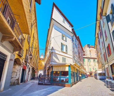 The medieval architecture on Via Cesare Beccaria with restored corner house, shabby facades of buildings, astronomical clock and restaurants, Brescia, Italy