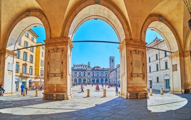 BRESCIA, ITALY - APRIL 10, 2022: The busy pedestrian Loggia Square from the portico of Palazzo della Loggia palace with tall stone arches, on April 10 in Brescia