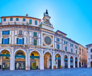 Walk down the medieval Piazza della Loggia square with a view on Torre dell'Orologio tower with historic astronomical clock, Brescia, Italy