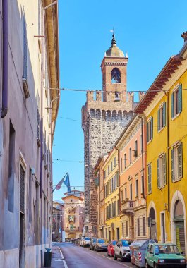 The narrow Via della Pace Street with line of historic houses and medieval Pallata Tower in background, Brescia, Italy