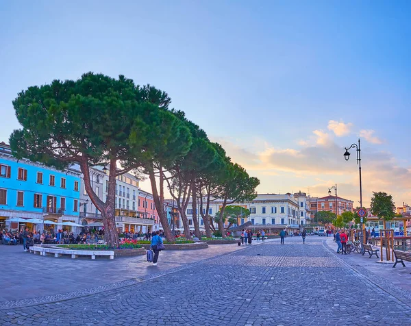 DESENZANO DEL GARDA, ITALY - APRIL 10, 2022: The evening embankment of Lake Garda with old houses, restaurants, spread pines and flower beds, Lungolago Cesare Battisti, on April 10 in Desenzano del Garda
