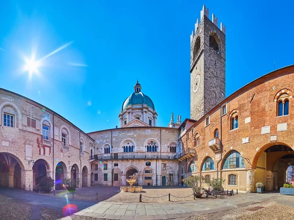 Panoramic view of Palazzo Broletto courtyard with Torre del Pegol clocktower, stone fountain and dome of New Cathedral in background, Brescia, Italy