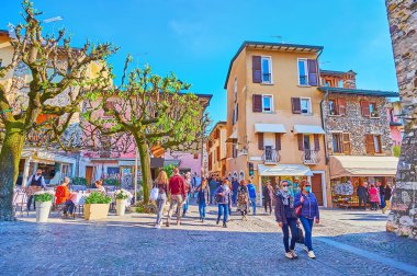 SIRMIONE, ITALY - APRIL 10, 2022: The line of spread trees in front of outdoor restaurants on Piazza Porto Valentino square in Sirmione old town, on April 10 in Sirmione