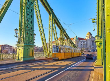 Budapeşte, Macaristan 'ın tarihi Budapeşte semtinin tarihi binalarına karşı sarı bir tramvayla gün doğumunda Özgürlük Köprüsü.