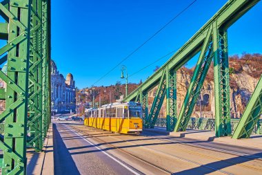Güzel sarı tramvay, Budapeşte, Macaristan 'daki Budapeşte bölgesinden Budapeşte' ye kadar olan klasik yeşil Libarty Köprüsü 'nde ilerliyor.