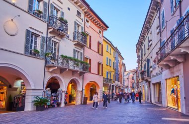 DESENZANO DEL GARDA, ITALY - 10 Nisan 2022: 10 Nisan 'da Desenzano del Garda' da tarihi evler, butikler, kafeler ve hediyelik eşya dükkanlarıyla dolu dar yaya geçidi Via Generali Achille Papa