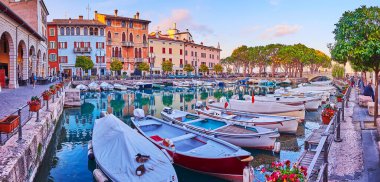 Ortaçağ evleri, kafeler ve restoranlarla dolu tarihi Porto Vecchio (Eski Liman) panoramik manzarası yayılmış çamlar ve günbatımı gökyüzü manzaralı Desenzano del Garda, Garda Gölü, İtalya