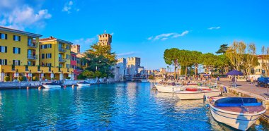 Sirmione limanının gök mavisi suları içinde küçük balıkçı tekneleri, renkli evler ve Scaligero Kalesi, İtalya