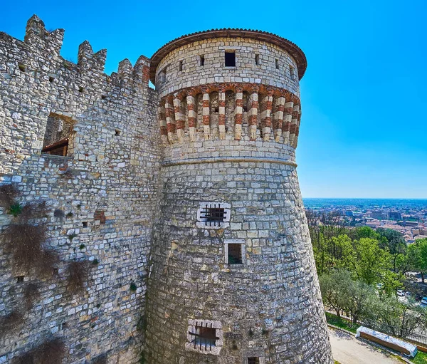 The medieval stone wall and tall Torre dei Prigionieri tower, Brescia Castle against the city skyline, Italy