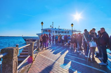 SIRMIONE, İTALYA - 10 Nisan 2022: 10 Nisan 'da Sirmione' de, gün batımında Garda Gölü 'ndeki küçük feribotta insanların sıralanması