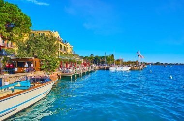Sirmione feribot iskelesinden Garda Gölü 'nün parlak mavi dalgalı yüzeyi ayrılan gemiyi ve İtalya' nın göl kıyısındaki farklı konteynırların bayrak sallama çizgisini görüyordu.