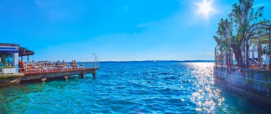 Parlak mavi gökyüzü, akşam güneşiyle Garda Gölü 'nün üzerinde, gök mavisi dalgalanan güneş yolu Sirmione, İtalya
