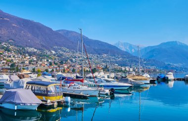Maggiore Gölü 'nde demirli tekne ve yatlar Alp yamaçları ve arka planda küçük evler, Locarno, İsviçre