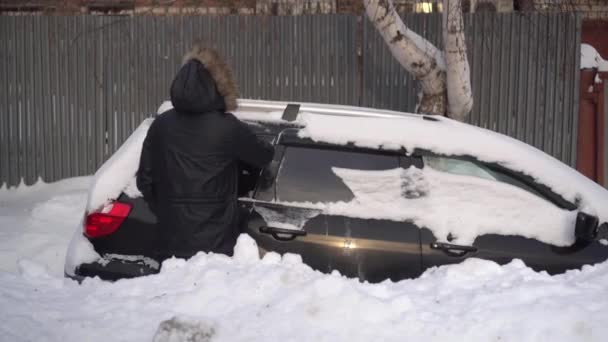 Молодой человек в пиджаке чистит свою машину от снега щеткой. Машина была покрыта снегом. Погодная катастрофа. — стоковое видео