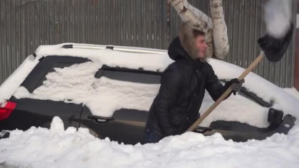 A young man in a jacket digs his car out of a snowdrift with a shovel. The car was covered in snow. Weather disaster. — Stock Video