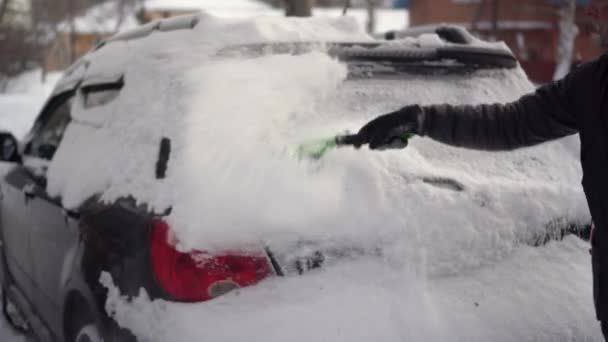 Un homme nettoie l'arrière de sa voiture de la neige avec un gros plan brosse. La voiture était couverte de neige. Catastrophe climatique. — Video