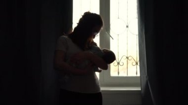 Genç bir anne, bir çocuğun kollarını pencerenin arka planına dayar. Pencereden gelen ışık, yeni doğmuş bir bebeği olan bir kadının görüntüsünü aydınlatıyor..