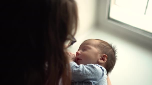 Een jonge moeder houdt een kind in haar armen tegen de achtergrond van een raam. Uitzicht van bovenaf. — Stockvideo