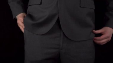 Takım elbiseli genç bir işadamı cebinden bir telefon çıkarır ve onunla konuşur. Siyah arka planda bir adamın beline yakın çekim.