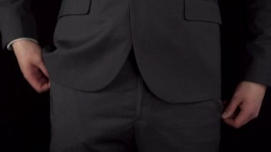 Takım elbiseli genç bir işadamı cebinden bir paket dolar çıkarıp elinde tutuyor. Siyah arka planda bir adamın beline yakın çekim.
