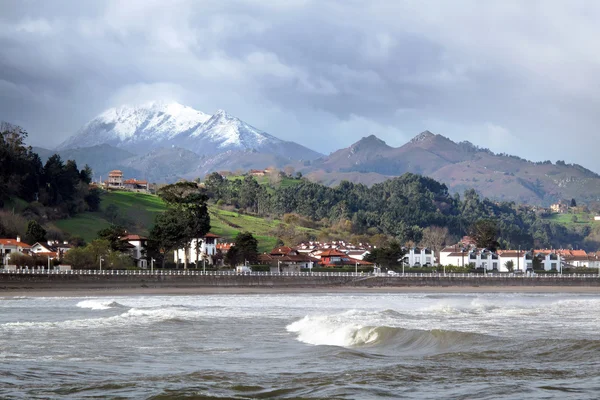 Ribadesella beach med stormigt moln och snötäckta berg — Stockfoto