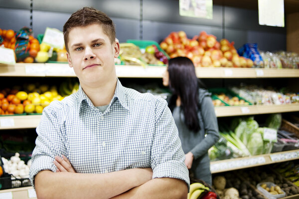 Молодой человек стоит перед полками магазинов
