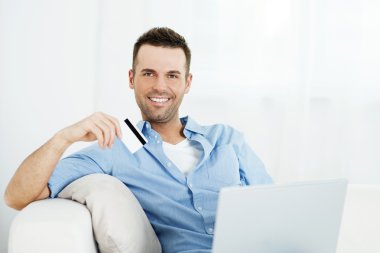 Adam kredi kartı tutuyor ve laptop kullanıyor.