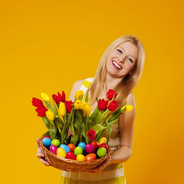 Mujer feliz sosteniendo cesta con flor de primavera y huevos de Pascua —  Fotos de Stock