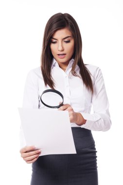 Shocked woman looking through a magnifying glass on documents