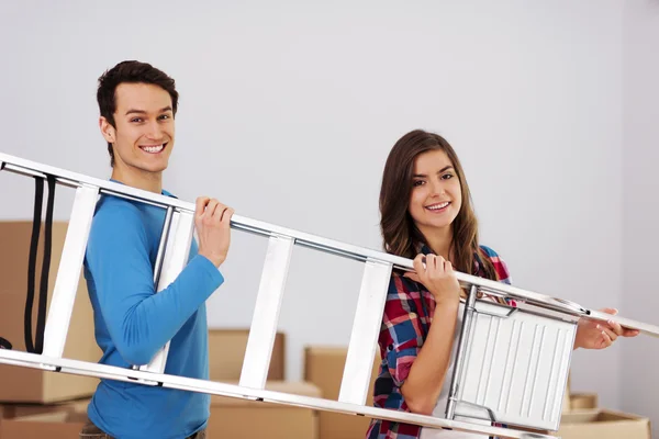 Jonge gelukkige paar met een ladder tijdens het bewegen in nieuwe huis — Stockfoto