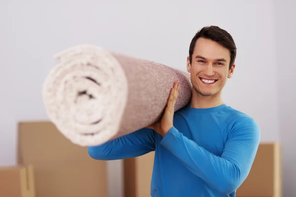Happy male carrying a carpet in new home — Stock Photo, Image