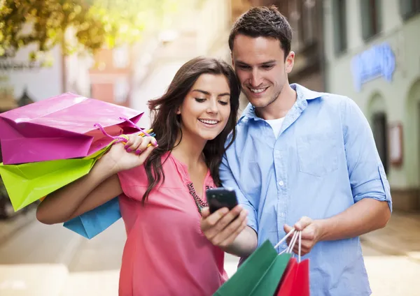 Jeune couple avec sac à provisions utilisant un téléphone mobile — Photo