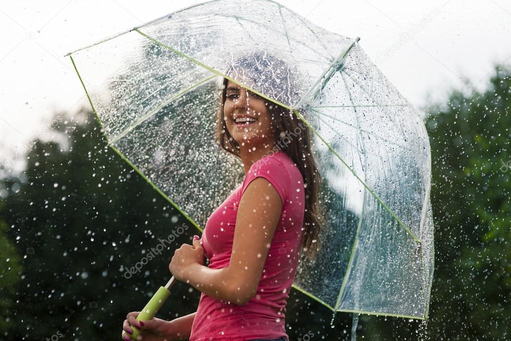 Young woman standing in summer rain with umbrella