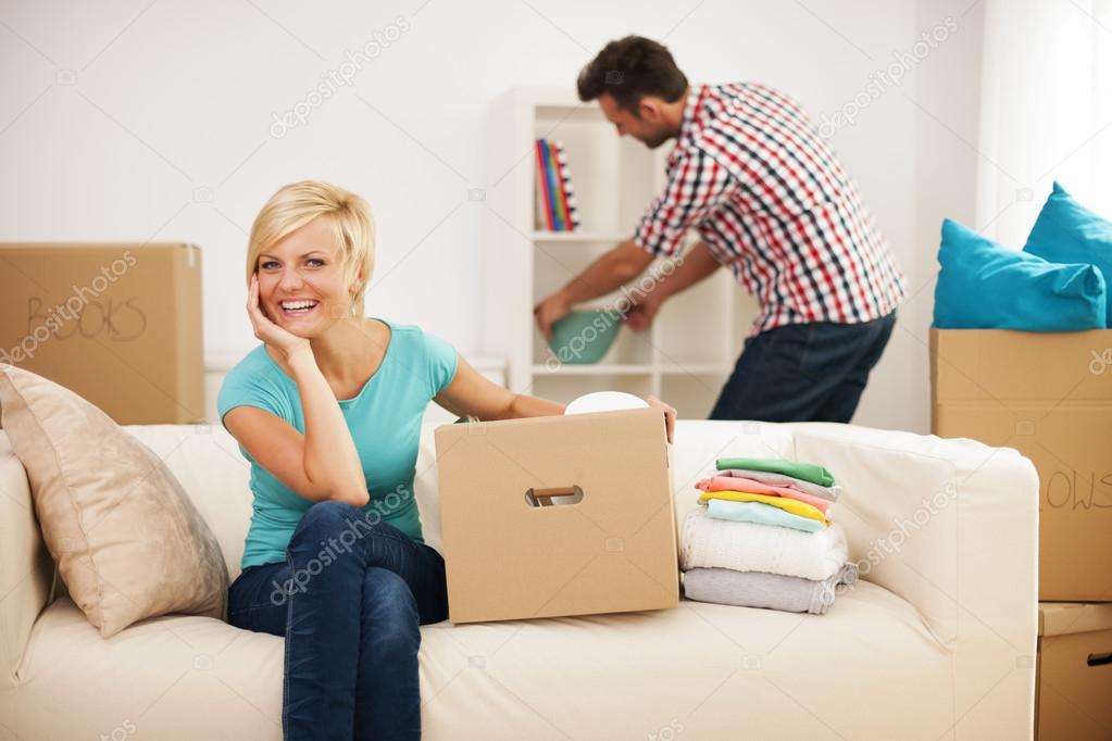 Beautiful woman resting on couch while her husband decorating their new living room