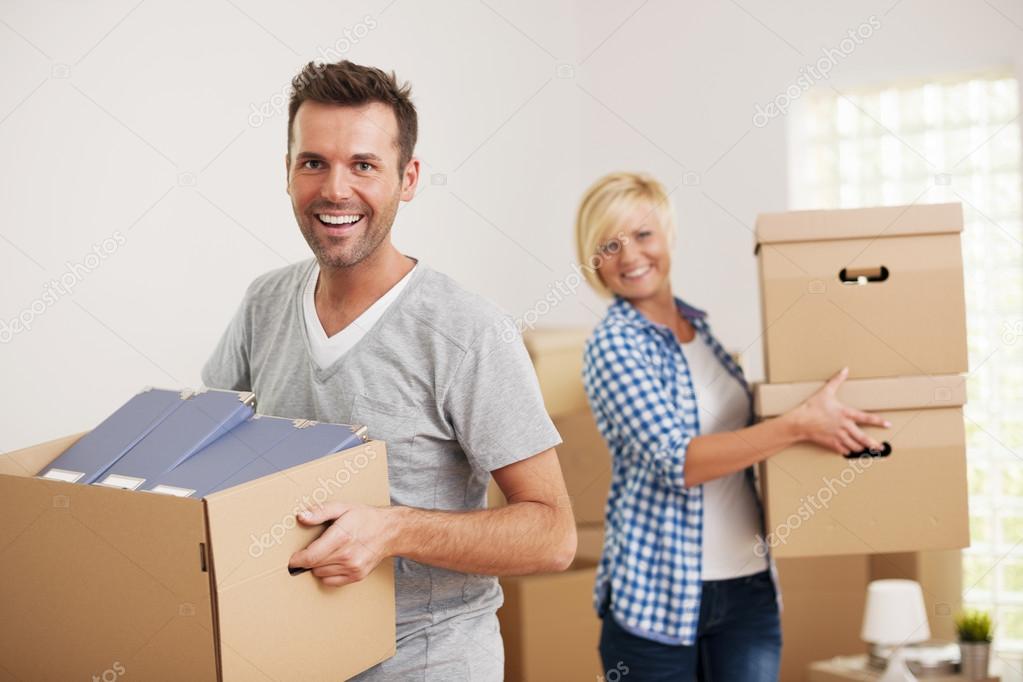 Couple carrying cardboard boxes in new home