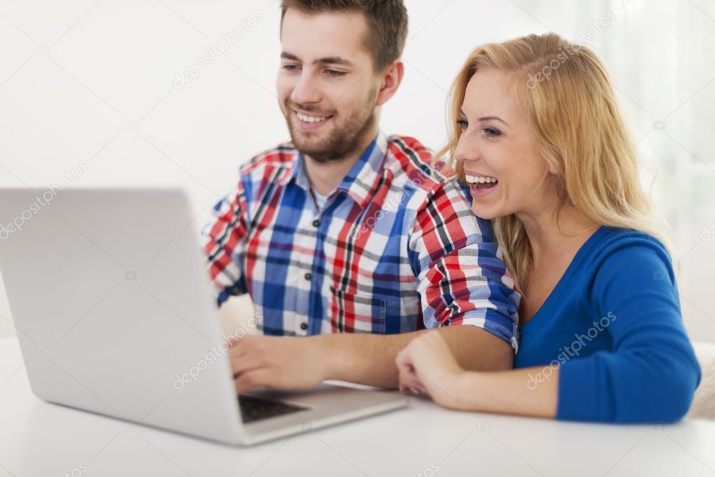 Laughing couple using computer at home