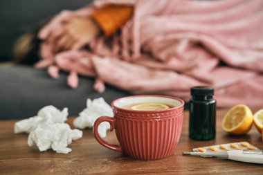 Arka planda, sıcak çay, ilaç ve kanepede yatan hasta kadının görüntüsü. 