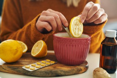 Bir kadın çay fincanına bir dilim limon koyuyor.