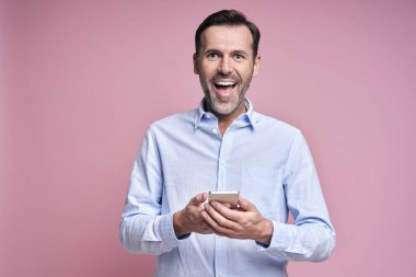 Elinde cep telefonu tutan gülümseyen adam.                               