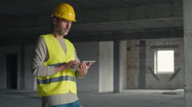 Kafkasyalı mühendis inşaat alanında dijital tablet üzerinde yürüyor ve geziniyor. 8K 'da kırmızı helyum kamerayla çekildi.     