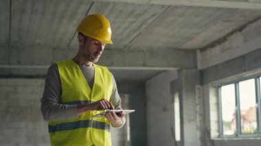 Kafkas mühendisi inşaat alanında dijital tablet üzerinde duruyor ve geziniyor. 8K 'da kırmızı helyum kamerayla çekildi.    