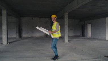 Kafkasyalı mühendisin inşaat sahasında yürüdüğü ve bina planlarına göz attığı geniş bir görüntü. 8K 'da kırmızı helyum kamerayla çekildi.