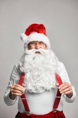 Beyaz Noel Baba dans ediyor ve kırmızı pantolon askısı tutuyor.