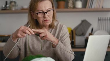 Evde kıdemli beyaz kadın video dersinden örgü örmeyi öğreniyor. 8K 'da kırmızı helyum kamerayla çekildi.   
