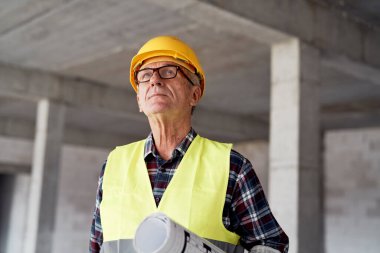 Kafkas kıdemli mühendis planları tutuyor ve şantiyeye bakıyor.