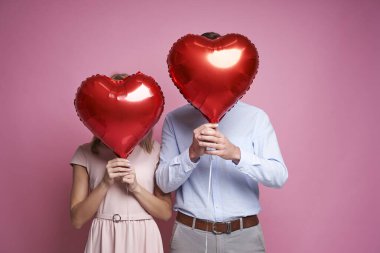 A couple hidden behind a heart shape balloons