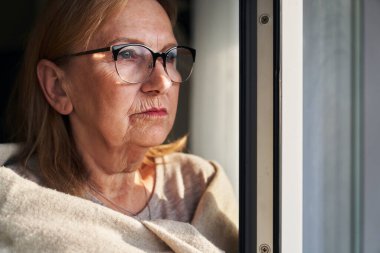 Caucasian senior woman with depression looking throw the window 