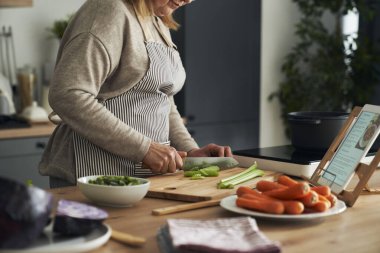 Unrecognizable caucasian senior woman cutting vegetables while cooking in the kitchen