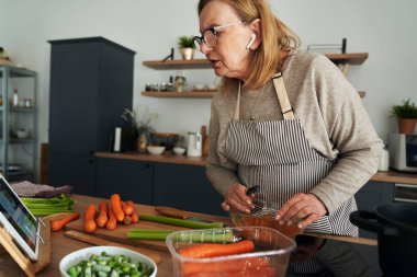 Caucasian senior woman cooking and chatting via earphones