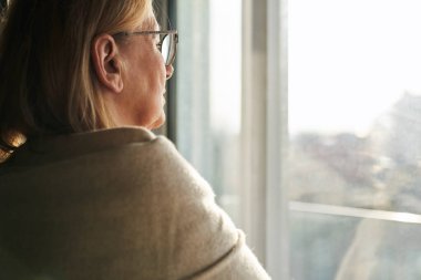 Caucasian senior woman with depression looking throw the window 